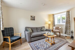 A living room with a grey sofa, a plaid armchair, a small table with a teapot, and a patterned rug. - 2 Bed in Chideock (oc-c36616) (Chideock)