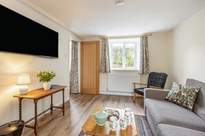 Ein Wohnzimmer mit einer Couch, einem Tisch mit Teekanne und Tassen, einem Fernseher und einem Fenster mit Vorhängen.