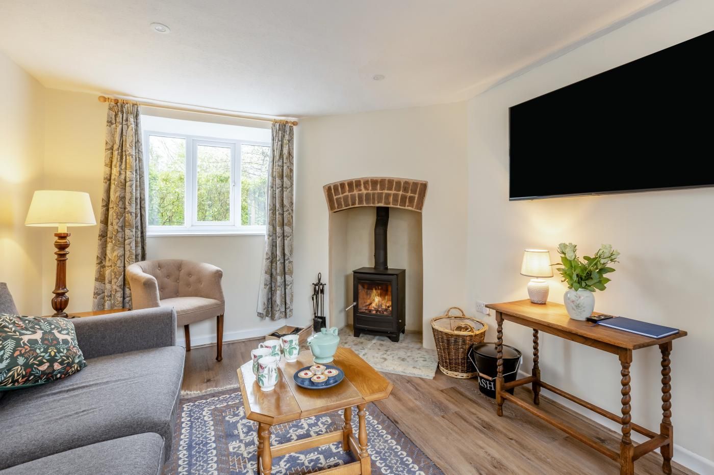 A cozy living room with a fireplace, a sofa, a table with a tray of snacks, and a television mounted on the wall.