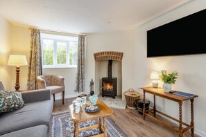 A cozy living room with a fireplace, a sofa, a table with a tray of snacks, and a television mounted on the wall. - 2 Bed in Chideock (oc-c36616) (Chideock)