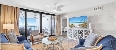 Una sala de estar moderna con un sofá azul, una mesa de centro de vidrio y un televisor sobre un mueble blanco.