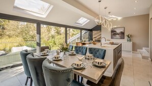 Een moderne keuken met een eethoek, grote ramen en uitzicht op groen.