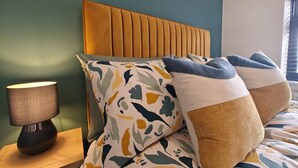 Ein Bett mit Holz Kopfteil, mehreren Kissen, einer Nachttischlampe und einer grünen Wand.