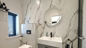 Ein Badezimmer mit Toilette, Waschbecken mit Spiegel und Fenster mit Jalousien.