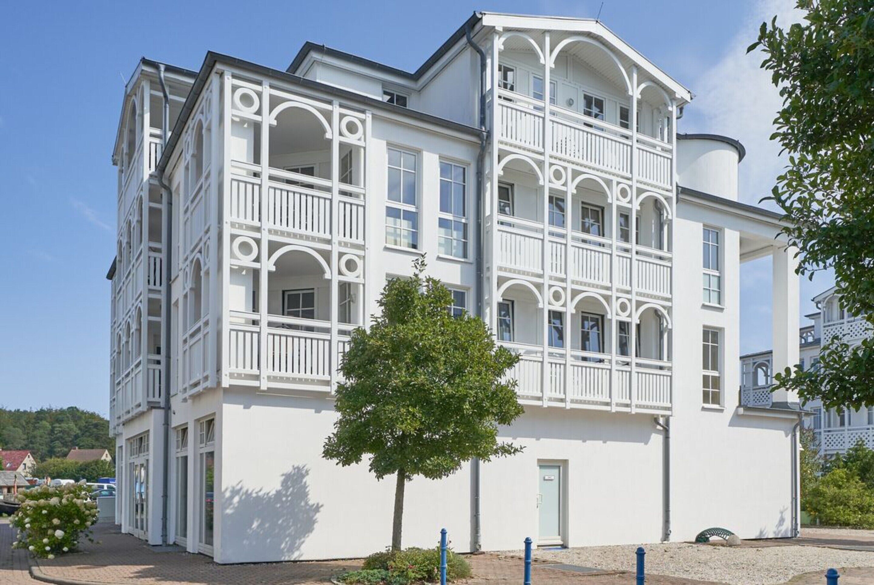 A white multi-story building with balconies, a door, and a tree in front.