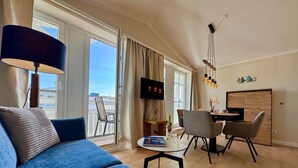 Uma sala de estar moderna com um sofá azul, área de jantar com cadeiras, televisão e vista para uma varanda.