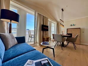 A modern living room with a blue sofa, a dining area with chairs, a TV, and a balcony view. - Ferienwohnung Ostseenah mit Balkon und Ahoi-rabatt (Sellin)