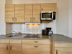 A kitchen with wooden cabinets, a stainless steel sink, a microwave, and a coffee maker. - Ferienwohnung Ostseenah mit Balkon und Ahoi-rabatt (Sellin)