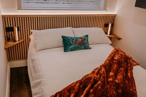 A bed with a wooden headboard, a teal pillow, and a brown blanket. - 2 Bed in Colwyn Bay (oc-b36345) (Colwyn Bay)