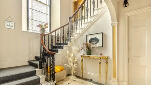 A grand staircase with ornate railings, a console table with a vase, and a basket of yellow towels. - 4 Bed in Barnstaple (oc-n34877) (Newton Tracey)