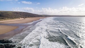 A coastal beach with waves, a sandy shore, and distant hills. - 4 Bed in Barnstaple (oc-n34877) (Newton Tracey)