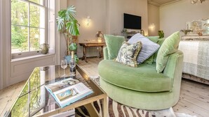 A living room with a green sofa, a glass coffee table, a plant, and a TV. - 4 Bed in Barnstaple (oc-n34877) (Newton Tracey)