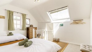 Een slaapkamer met twee bedden, een raam, een radiator, een houten dressoir, een kleine tafel en een kledingrek.