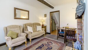 Een gezellige woonkamer met twee fauteuils, een tapij met dessin, een houten tafel en een spiegel aan de muur.