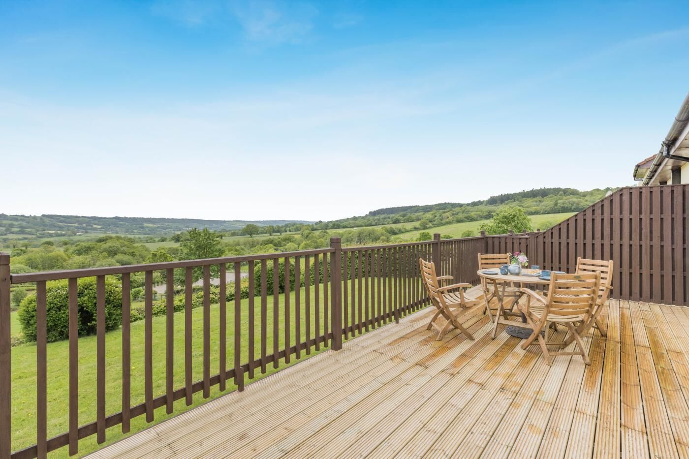 A wooden deck with a table and chairs, overlooking a green landscape.