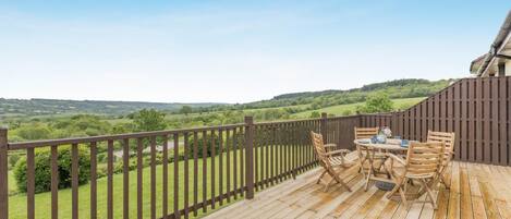 A wooden deck with a table and chairs, overlooking a green landscape.