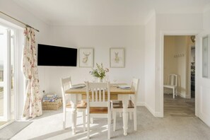 Ein Essbereich mit Holztisch, weißen Stühlen, einem an der Wand montierten Fernseher und gerahmten Bildern.