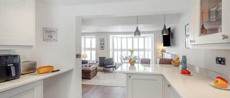 Una cocina moderna con armarios blancos, horno empotrado y una zona de comedor con mesa y sillas.