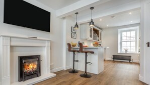 Ein modernes Wohnzimmer mit Kamin, Holzboden und einer Küchenzeile mit Barhocker.