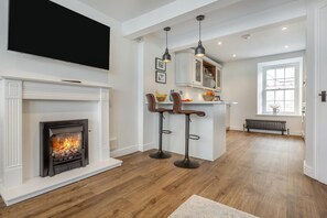 Ein modernes Wohnzimmer mit Kamin, Holzboden und einer Küchenzeile mit Barhocker.