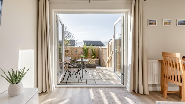 Et moderne værelse med en skydedør, der fører ud til en udendørs terrasse med bord og stole.