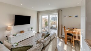 En moderne stue med et fladskærms-tv, en sofa, et spisebord med stole og en skydedør, der fører til et udendørs område.