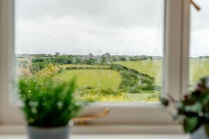 A view through a window with a rural landscape, including fields and a distant building. - 2 Bed in Padstow (oc-g34917) (Trevone)