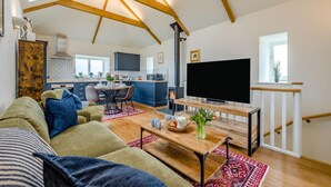 En moderne stue med sofa, sofabord og fjernsyn. Et køkken med komfur og skabe ses i baggrunden.