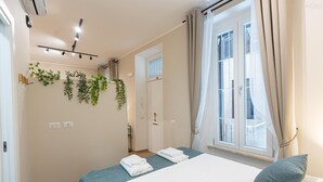 A bedroom with a bed, two towels, a window with curtains, a ceiling fan, and wall-mounted plants. - Red Hat Home by Campo de Fiori (Rome)