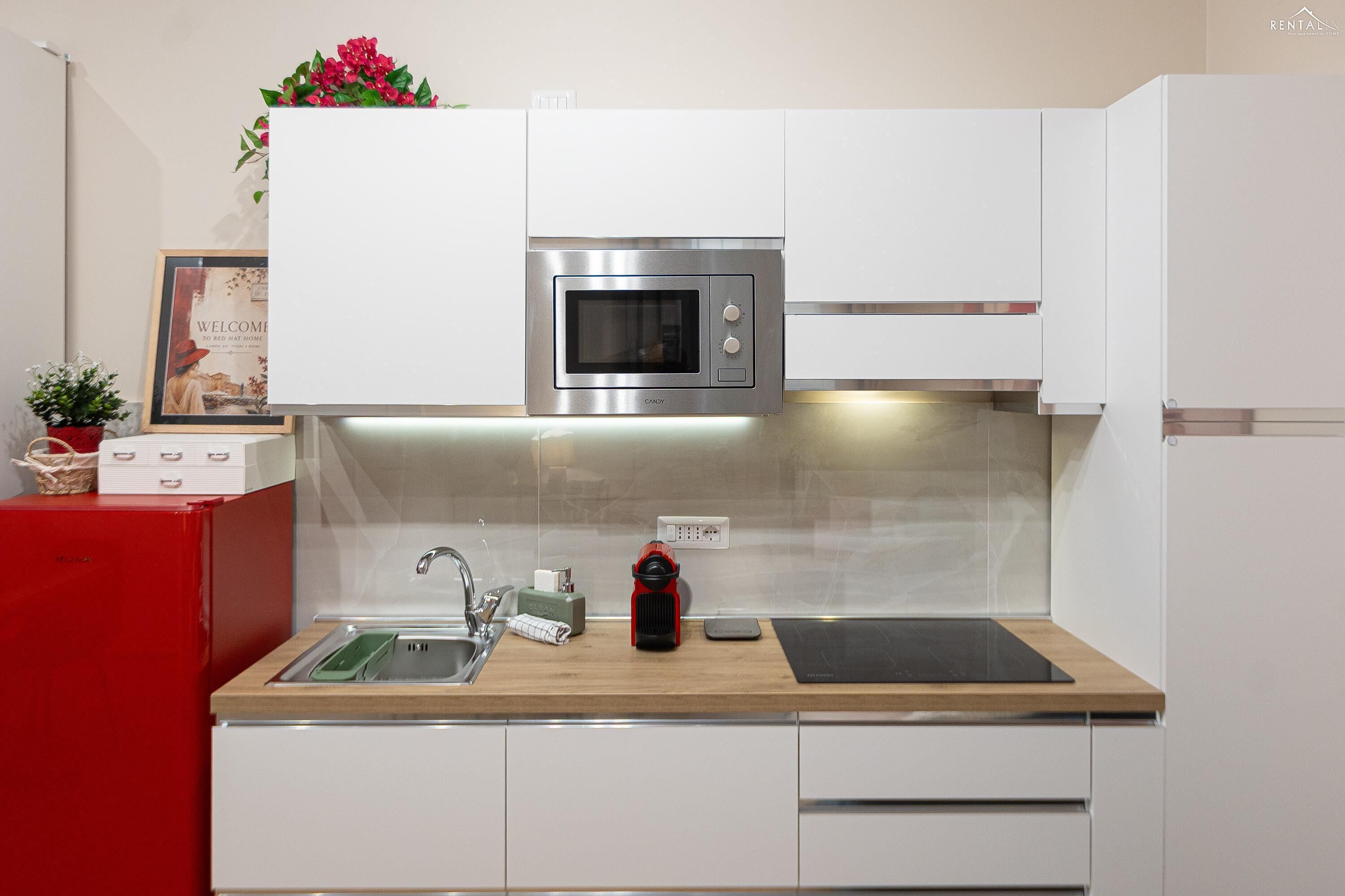 A modern kitchen with a built-in microwave, a sink, a red appliance, and a countertop with a red object.