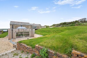 A modern house with a stone exterior, a wooden deck, and a grassy yard. - 2 Bed in Padstow (oc-f34918) (Trevone)