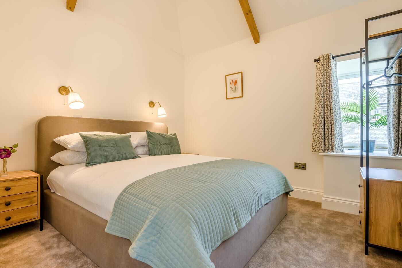 A bedroom with a bed, bedside table, lamp, and window with curtains.