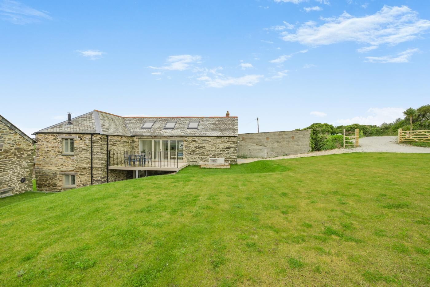 A stone house with a large grassy yard, a wooden gate, and a clear sky.