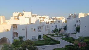 A courtyard with white buildings, paved walkways, and greenery. - résidence Nesrine-Hammemet sud (Hammamet)
