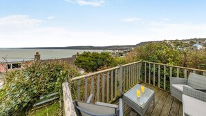 Eine Terrasse mit Korbmöbeln und einem Glastisch mit Blick auf eine Küstenstadt und das Meer.