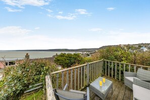 Eine Terrasse mit Korbmöbeln und einem Glastisch mit Blick auf eine Küstenstadt und das Meer.