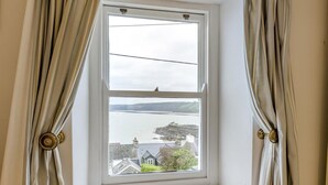 Ein Fenster mit Vorhängen, Blick auf ein Gewässer und Gebäude in der Ferne.