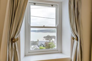 Ein Fenster mit Vorhängen, Blick auf ein Gewässer und Gebäude in der Ferne.