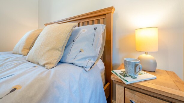 Una cama bien hecha con almohadas, una mesita de noche con una lámpara y un libro.