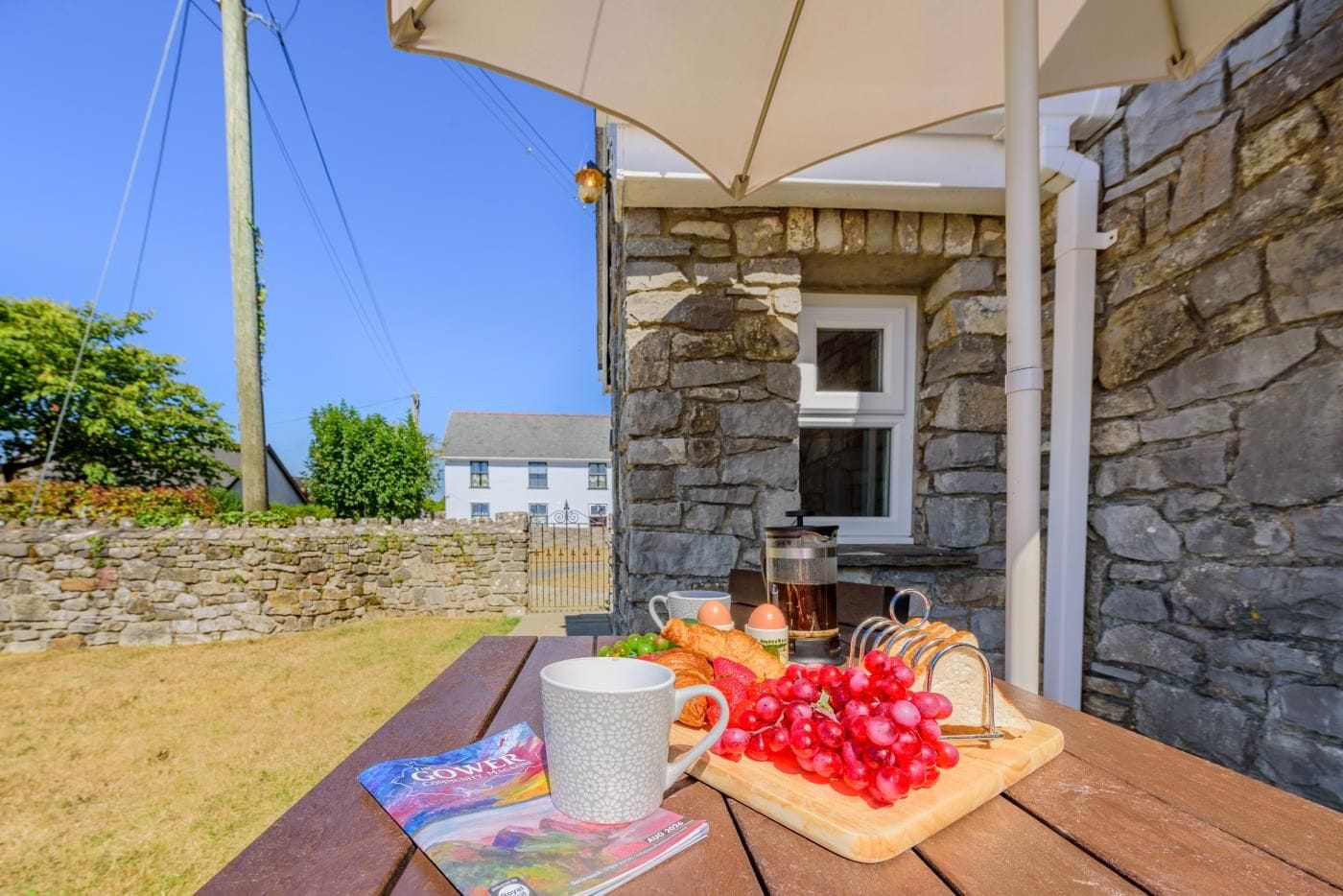 A stone building with a wooden table set for breakfast, including eggs, bread, and fruit.