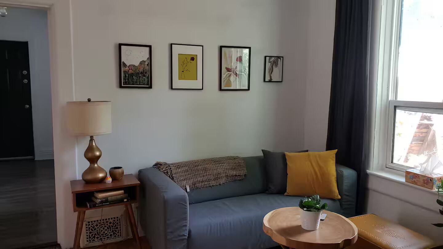 Ein Wohnzimmer mit einer Couch, einer Lampe, einem kleinen Tisch und einem Fenster mit Vorhängen.