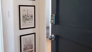 A hallway with framed cityscape pictures on the wall, a wooden floor, and a dark door. - Winnipeg Centre Main Floor Apartment #1. Pet Friendly! (Winnipeg)