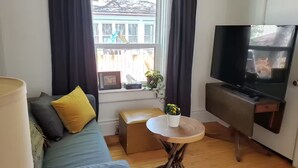A living room with a sofa, a small table with a plant, a television, and a window with curtains. - Winnipeg Centre Main Floor Apartment #1. Pet Friendly! (Winnipeg)