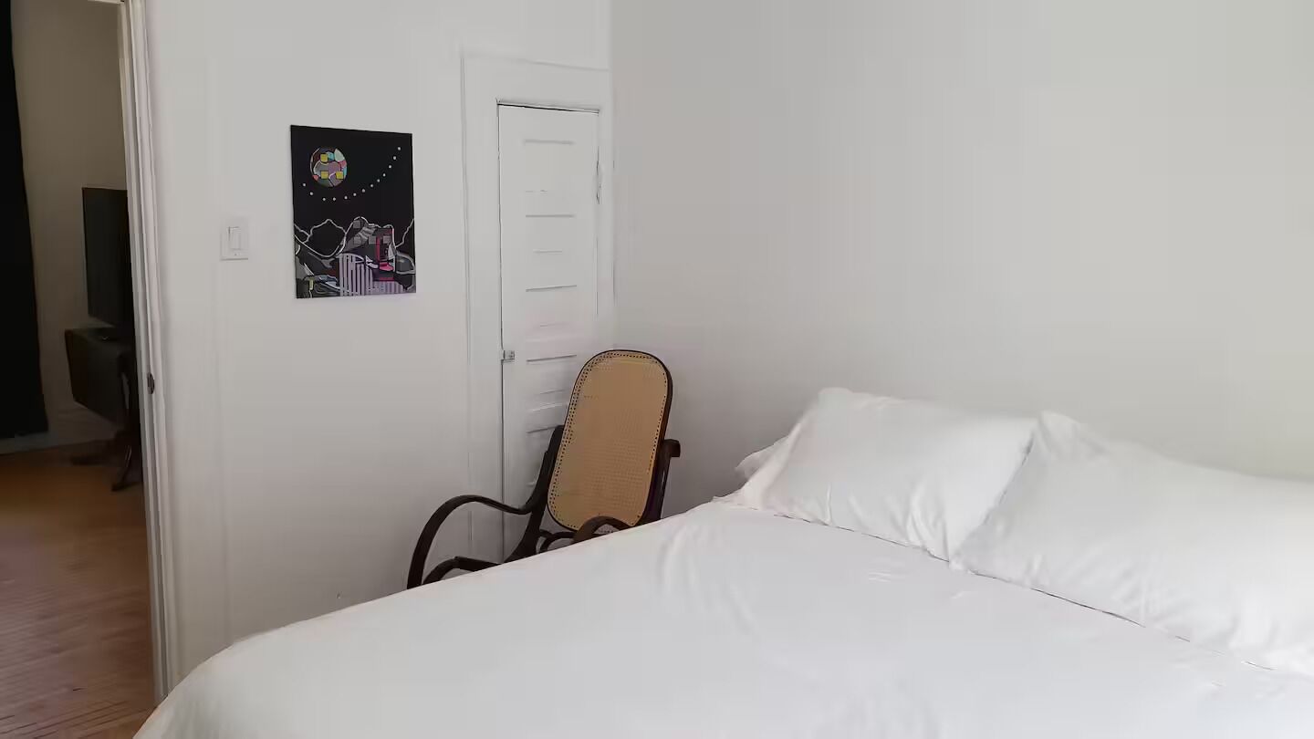 A bedroom with a bed, a chair, a door, and a wall-mounted artwork.