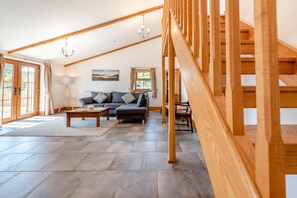 A spacious living area with a high ceiling, wooden beams, a staircase, and a view through large windows. - 3 Bed in Parkmill (oc-t36335) (Parkmill)