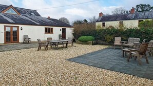 Ein Patio mit Tisch und Stühlen, befestigt mit Kies, und ein weißes Gebäude mit dunklem Dach.