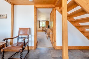 Un escalier en bois menant à un deuxième étage, une chaise au premier plan et une vue sur une pièce avec une fenêtre et une table.