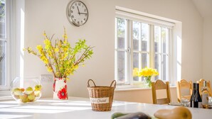 A kitchen with a clock, a vase with flowers, a basket, and fresh produce on the counter. - 3 Bed in Berwick St. John (oc-k36615) (Berwick Saint John)