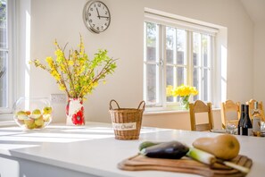 A kitchen with a clock, a vase with flowers, a basket, and fresh produce on the counter.