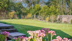 A well-maintained lawn with a stone pathway leading to a seating area, surrounded by lush greenery and trees. - 3 Bed in Berwick St. John (oc-k36615) (Berwick Saint John)